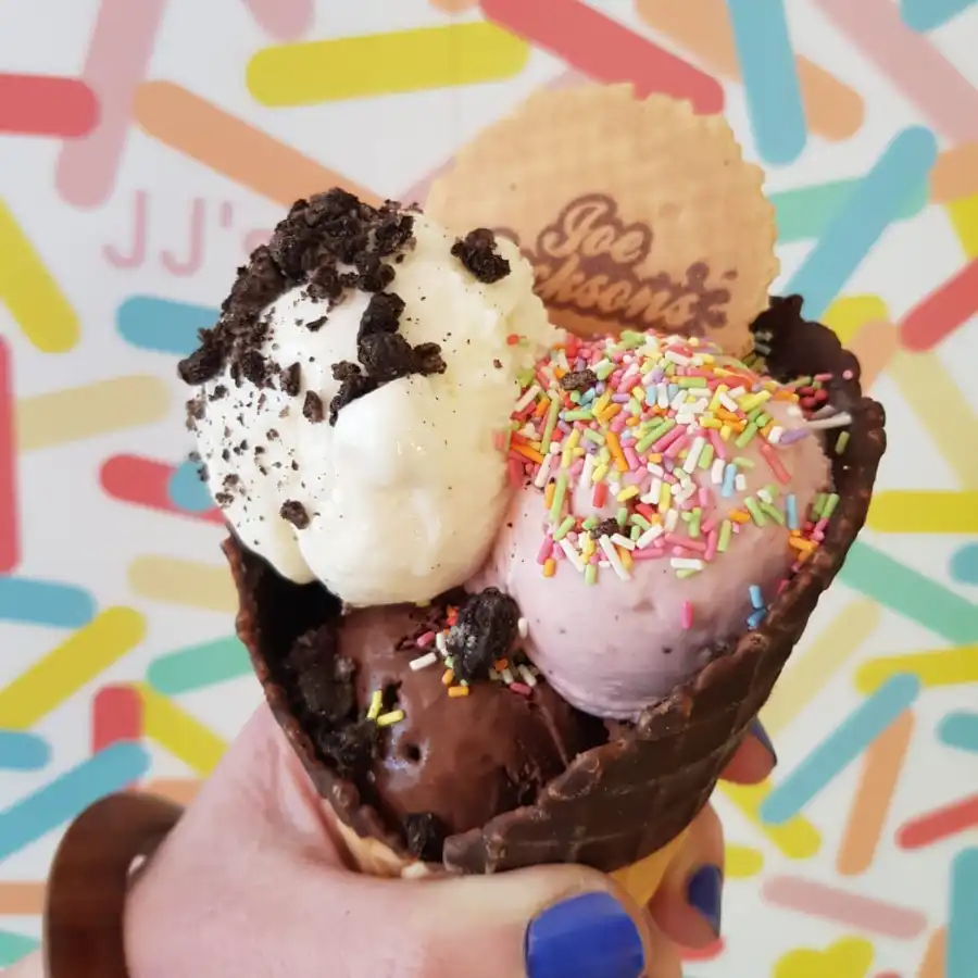 Vanilla, chocolate and strawberry scoop in a cone topped with rainbow sprinkles, brownie chunks and wafer with joe jackson name on it